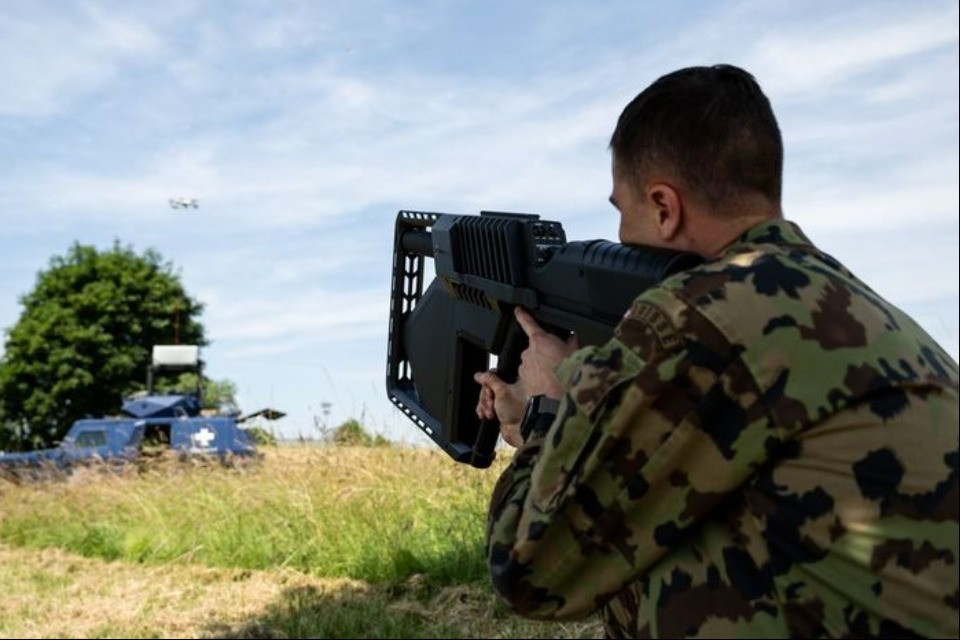 Un membro dell'esercito punta un Drone Gun Tactical di DroneShield contro un drone nel cielo. Questi sistemi sono utilizzati per interferire elettronicamente con i droni indesiderati o ostili e impedirne il controllo.  © DDPS